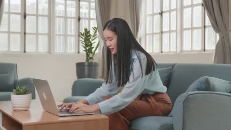 asian female working on laptop and smiling at living room, video in 4k