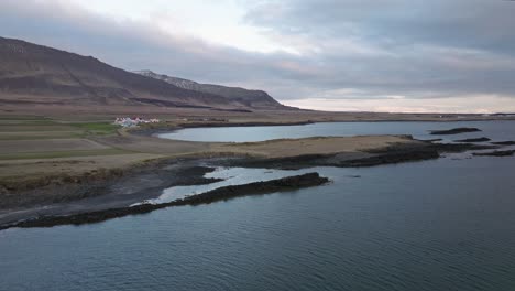 a peaceful coastal view near akranes, iceland, showcasing the rugged shoreline, calm waters, and distant houses beneath a cloudy sky at dusk