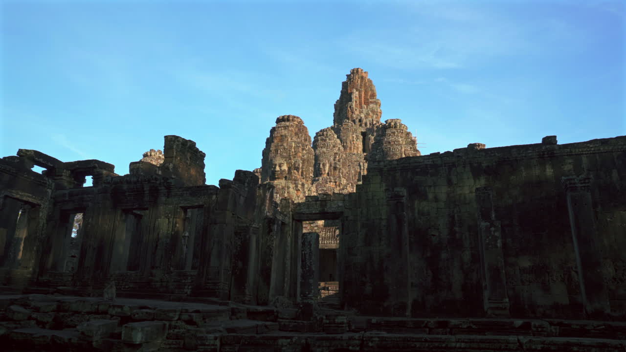 Wide angle establishing pan across Bayon temple carved faces bathed in warm golden light at dusk, no people nobody