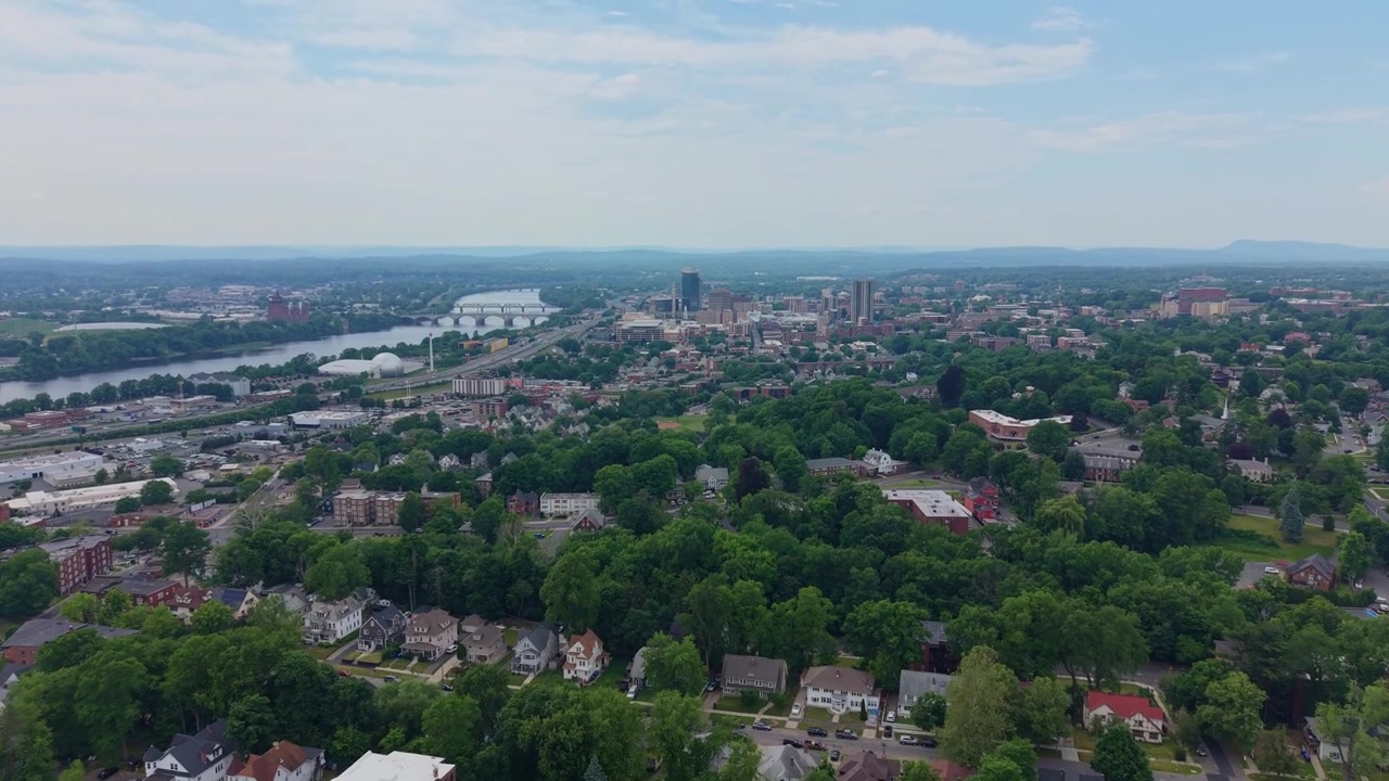 Vuelo de dron acercándose a Springfield al mediodía con un hermoso paisaje verde, elevando la cámara, vista épica del horizonte, Massachusetts.