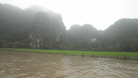 misty mountains and rice paddies reflected in the river under overcast skies in ninh binh vietnam