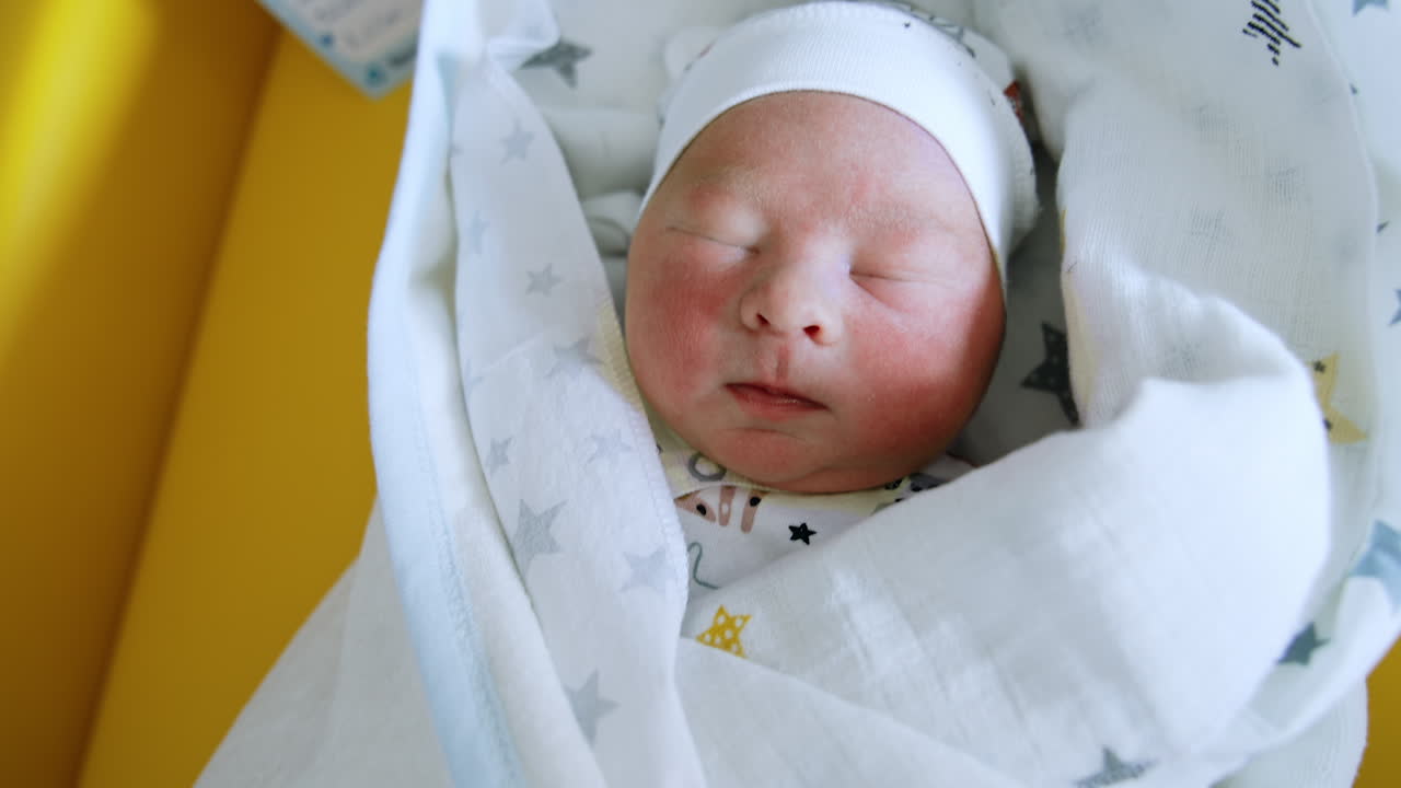 Cute newborn baby sleeping covered in blankets. Lovely child is winking from the light. Close up.