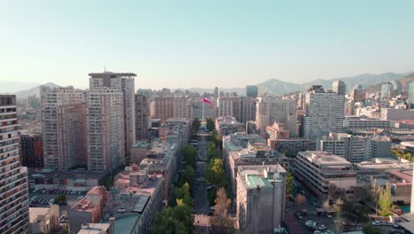 Vista-Aérea-Panorámica-De-Los-Edificios-De-Paseo-Bulnes-En-El-Centro-De-Santiago-Con-La-Bandera-Chilena-Al-Fondo,-Chile