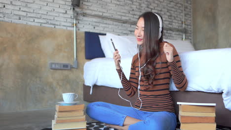 a young woman wearing headphones is sitting on the floor between piles of books, and a cup of coffee rocks out to the music from her smartphone