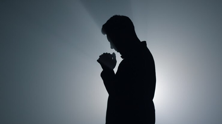Silhouette man asking god blessing in darkness. Male person praying indoors.