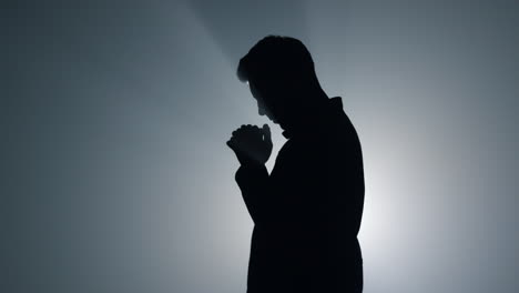 silhouette man asking god blessing in darkness. male person praying indoors.