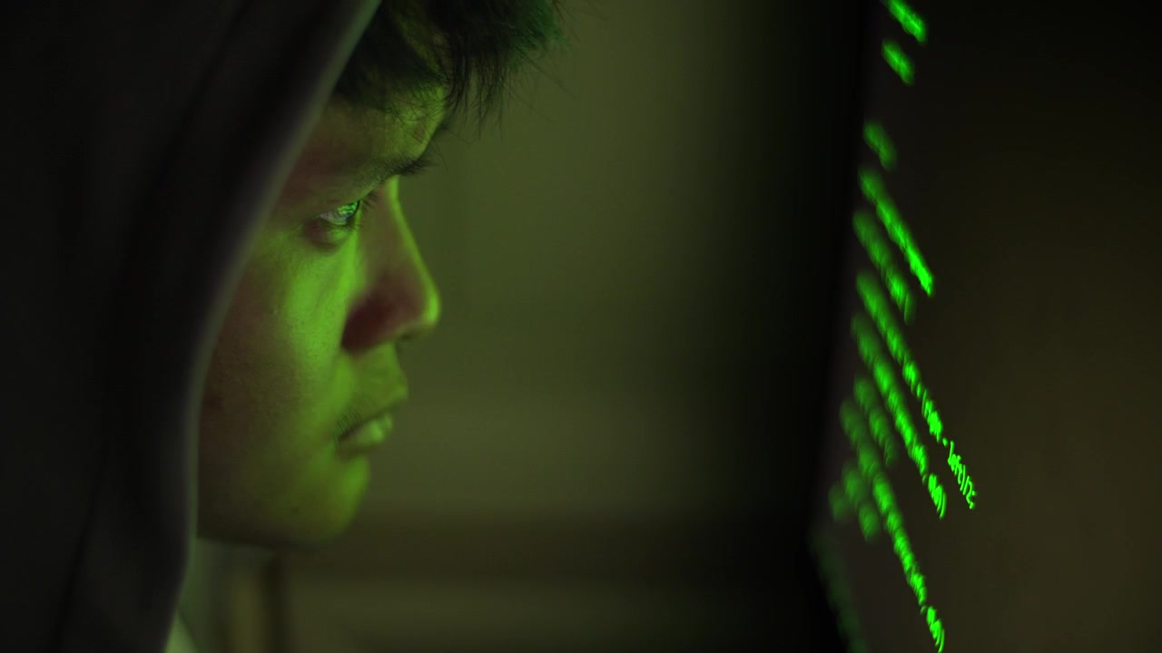 Nærbillede af asiatisk hacker i aktion i et mørkegrønt rum, cybersikkerhedskoncept