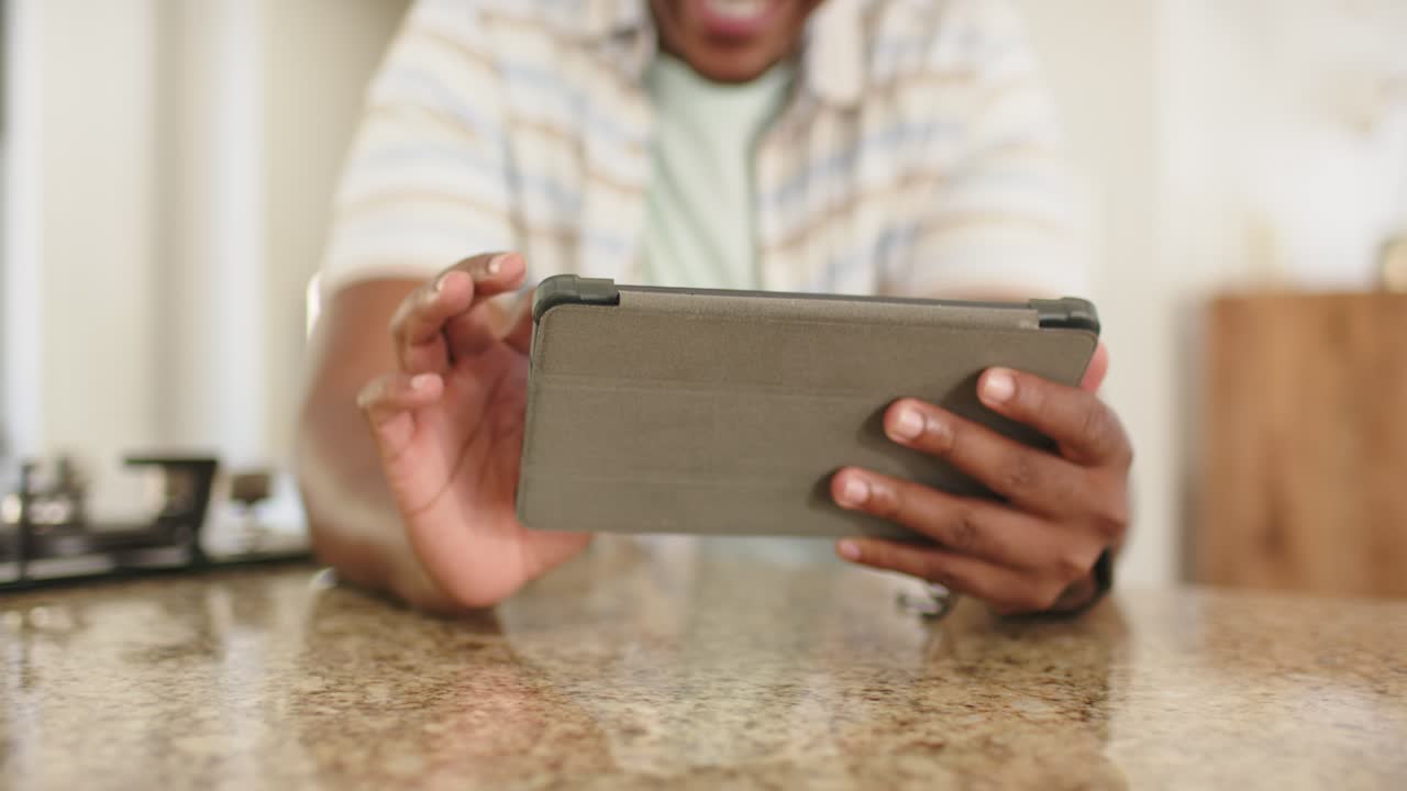 Adult male holding tablet in folio cover at kitchen counter, tapping and swiping to browse