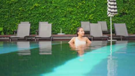 attractive asian woman resting in outdoor hotel swimming pool slomo