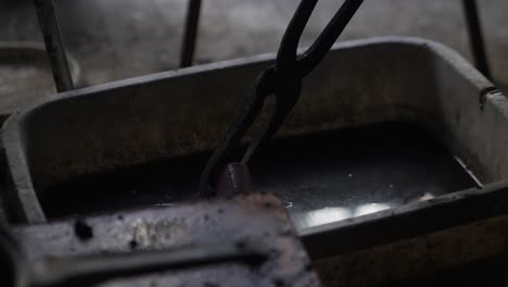 close-up of a blacksmith putting hot metal into water to cool, a process known as quenching