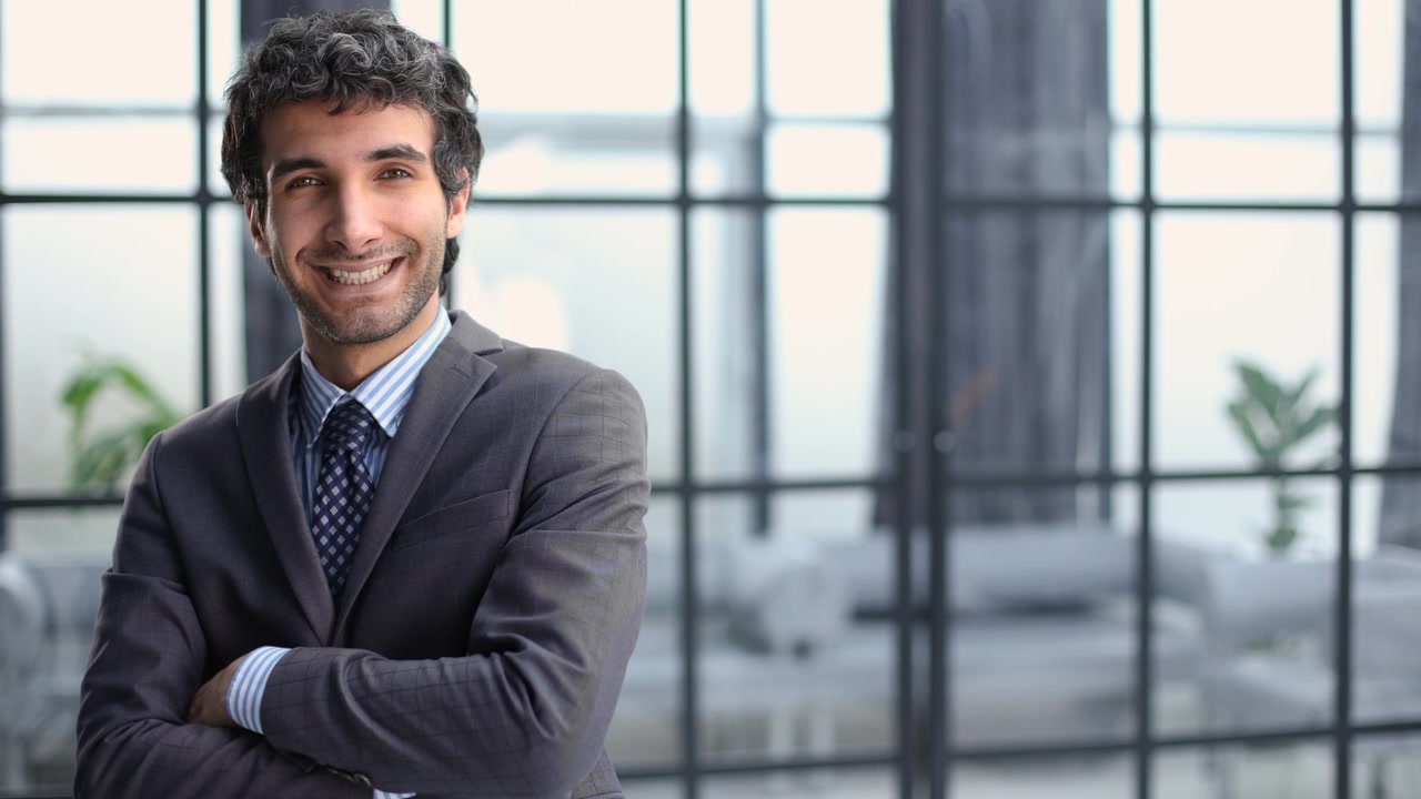 Giovane uomo d'affari sorridente e sicuro di sé con le braccia conserte in un ufficio moderno