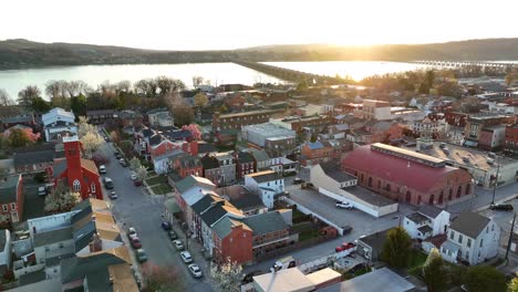 Drone-view-zooming-out-of-a-downtown-district-in-America-at-sunset-with-reflections-off-many-of-the-buildings-with-a-river-and-bridge-in-the-background