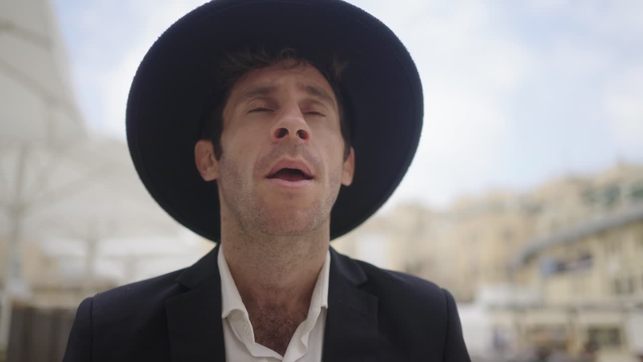 Jewish man praying at the Western Wall in Jerusalem, Israel. He wears a black hat and coat. Stabilized camera moves around subject in slow-motion with selective focus as he makes typical movements.