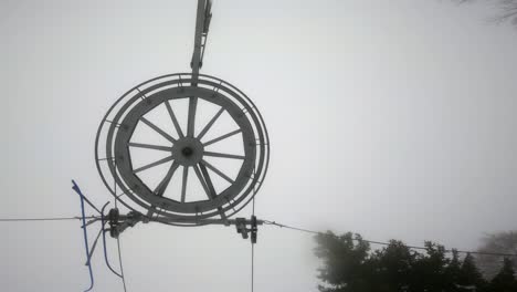 ski lift pulley, wires, and wheel against a cloudy and foggy sky