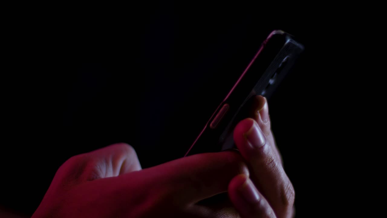 Thumb scrolling and typing on a smartphone close up in a dark room with red and white lighting