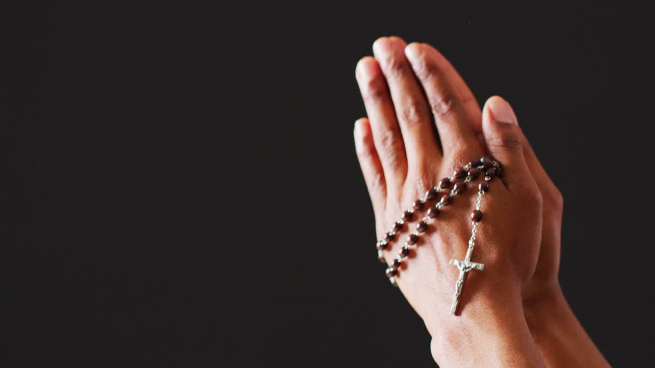 Mãos em oração com terço em fundo preto com espaço para texto