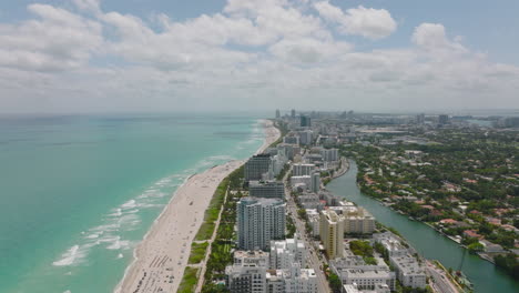 Absteigende-Panoramaaufnahmen-Aus-Der-Luft-Eines-Städtischen-Bezirks-An-Der-Küste.-Streifen-Von-Mehrstöckigen-Apartmentgebäuden-Und-Hotels-Am-Strand.-Miami,-USA