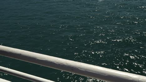 looking through the bar railings on a ferry crossing, line shimmers and sparkles on the surface of the ocean water as wind causes small waves and ripples