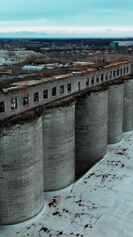 old chemical plant construction. ruined long warehouse build on the tops of high concrete reservoirs. modern industrial plant and city at the backdrop. vertical video