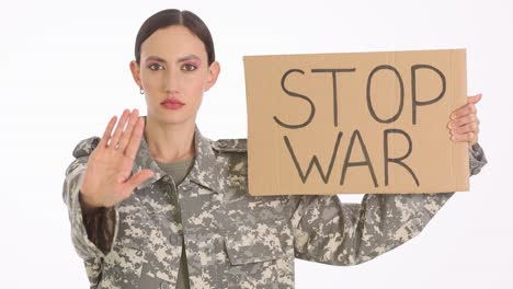 a woman in military uniform holds a "stop war" sign and makes a stop gesture