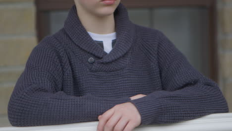 Portrait-of-teen-boy-at-home-on-front-porch-tilt-down-to-his-hands