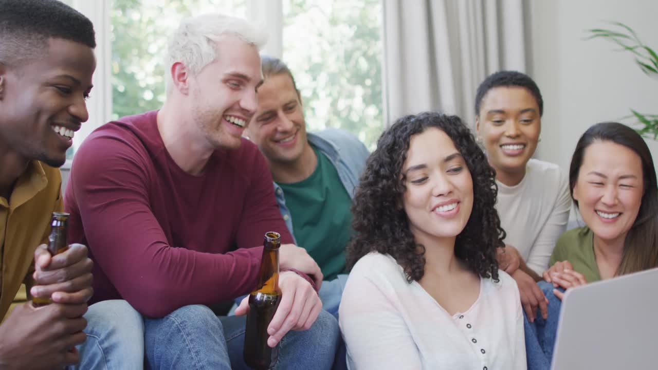 grupo diverso de amigos felices hombres y mujeres mirando la computadora portátil y riendo en la sala de estar