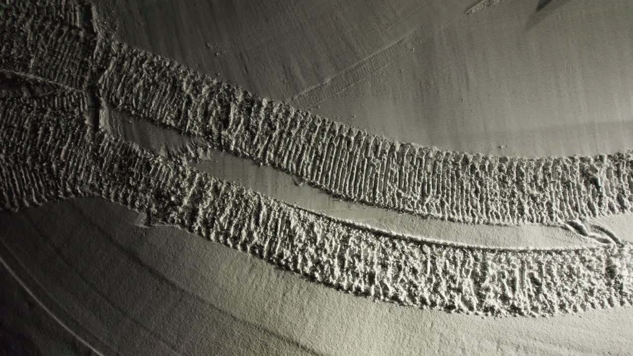Drone shot descends onto a snow groomer climbing a slope at night, revealing fresh tracks in snowy Andorran mountains.