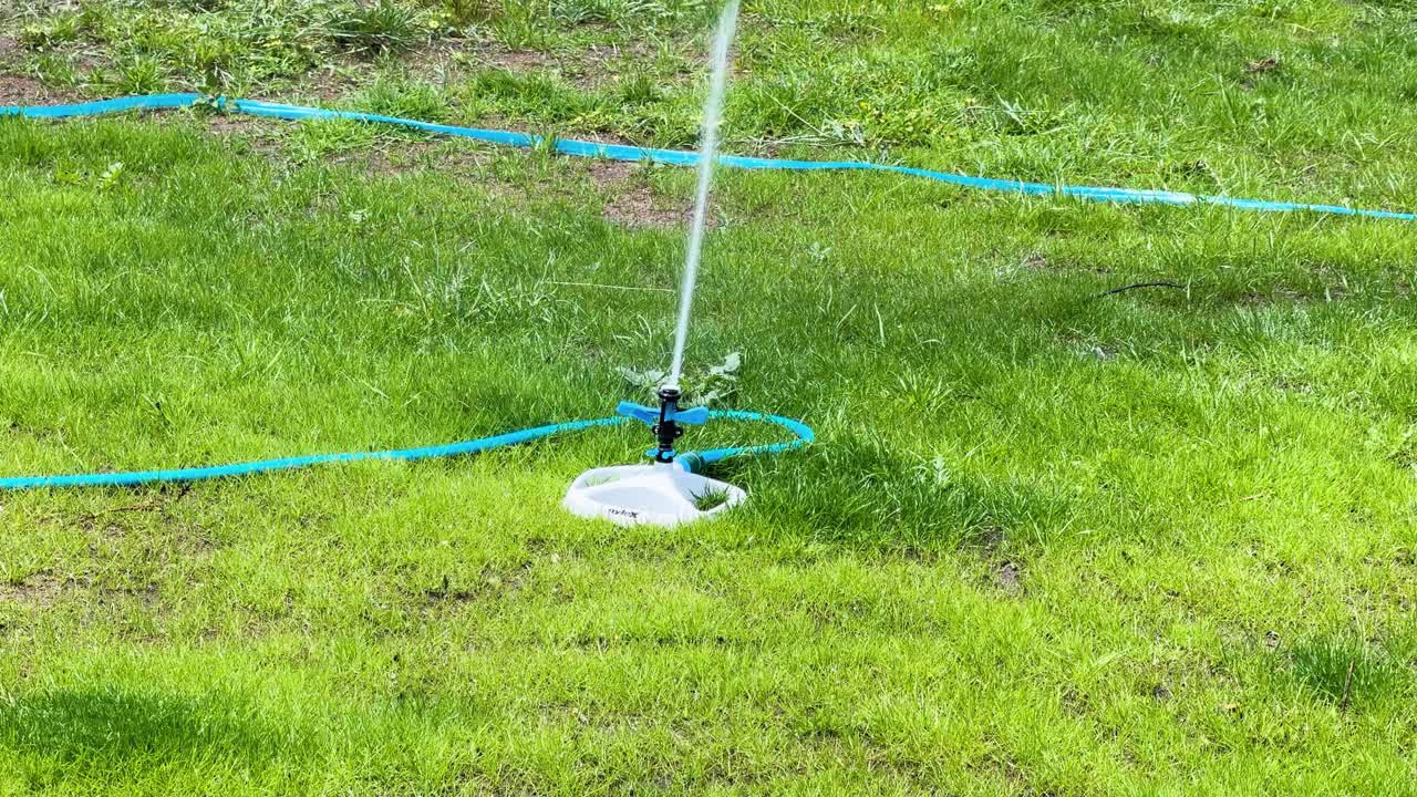 Slow motion rotating sprinkler waters bright green lawn on sunny day, wide static shot