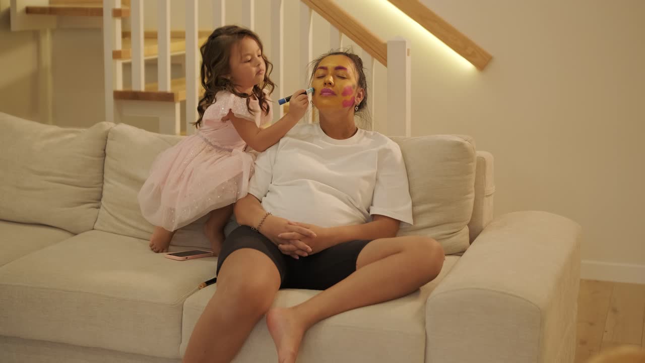 어린 소녀 가 가정 에서 임신 한 어머니 에게 메이크업 을 쓰고 있다