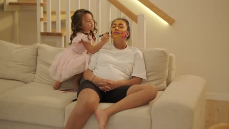 niña pequeña aplicando maquillaje a su madre embarazada en casa