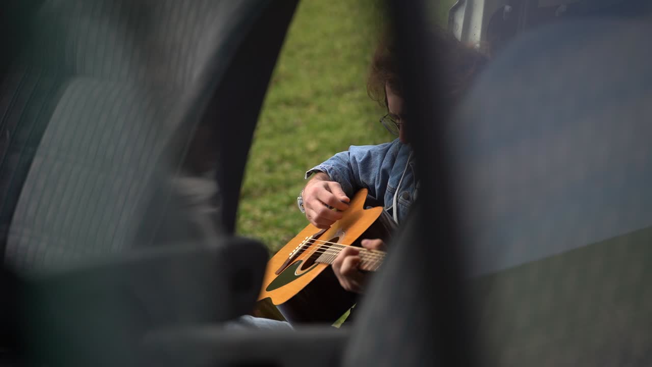 안경을 쓴 젊은 남자가 캐러밴 뒤에서 기타를 연주합니다.