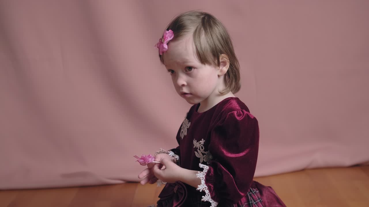 una niña linda en un vestido de borgoña vintage está jugando con un clip para el cabello