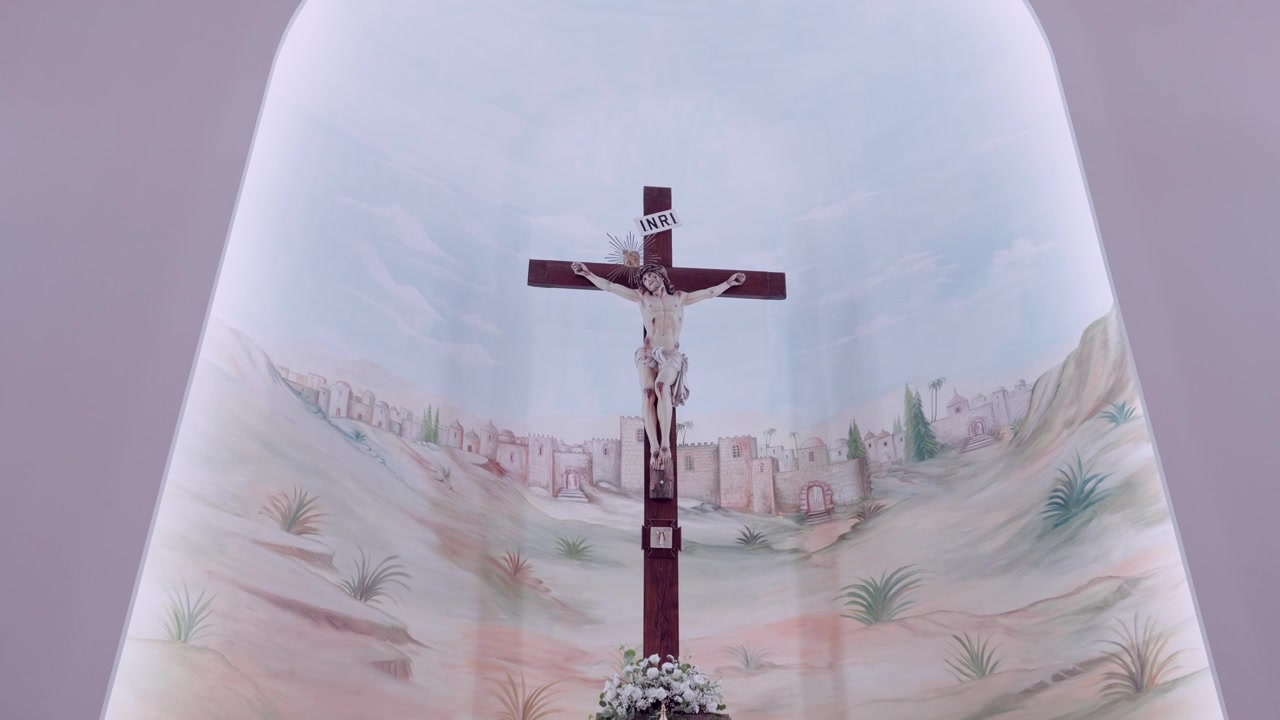 Crucifijo de madera montado sobre un mural pintado de las colinas de Jerusalén dentro del ábside de una iglesia