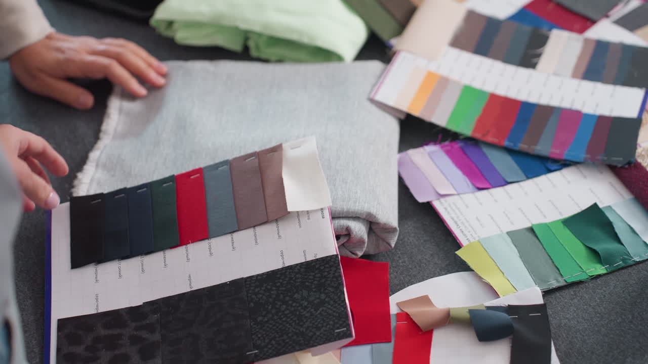 Fashion designers selecting fabric colors from vibrant color panels at creative workspace filled with colorful textile samples, folded fabrics, and pattern sheets for inspiring fashion projects