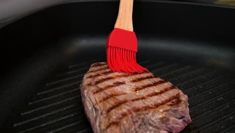 Nahaufnahme-Eines-Gebratenen-Steaks,-Das-Mit-Öl-Mit-Einer-Roten-Bürste-Mit-Bambusgriff-Für-Eine-Köstliche-Mahlzeit-Gebürstet-Wird