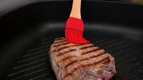 primer plano de un bistec frito cepillado con aceite con un cepillo rojo con mango de bambú para una comida deliciosa