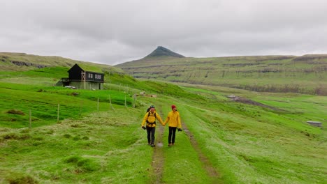two tourists in yellow jackets walk hand in hand on a grassy faroe islands trail