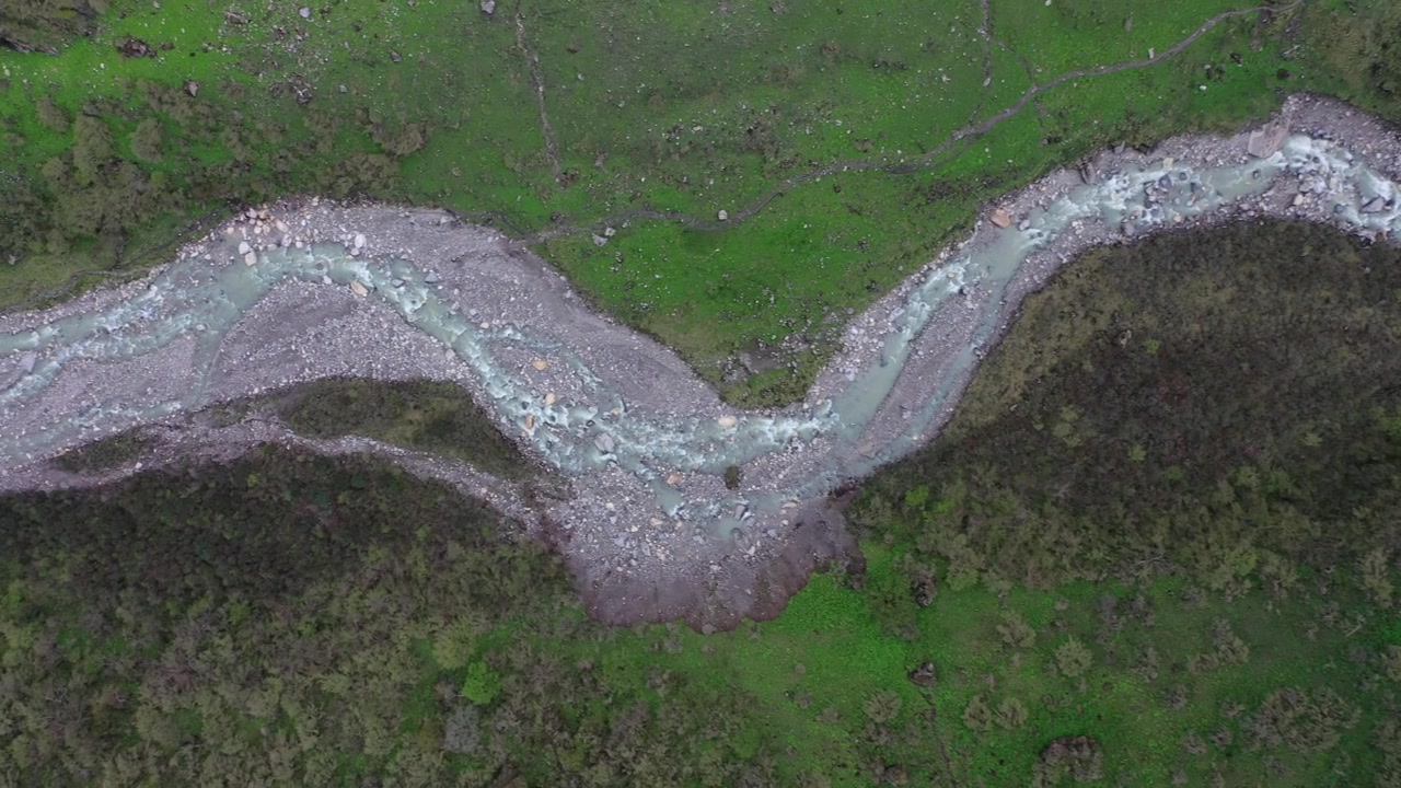 Breathtaking top-down aerial drone clip of a glacial river twisting through a rocky green mountain valley in Nepal. Showcases the rugged wilderness and natural beauty of the Himalayan landscape.