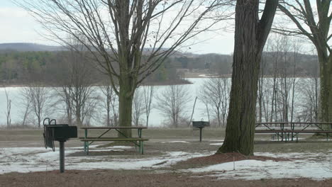 mesas de piquenique vazias no parque no inverno com lago na panela de fundo à direita