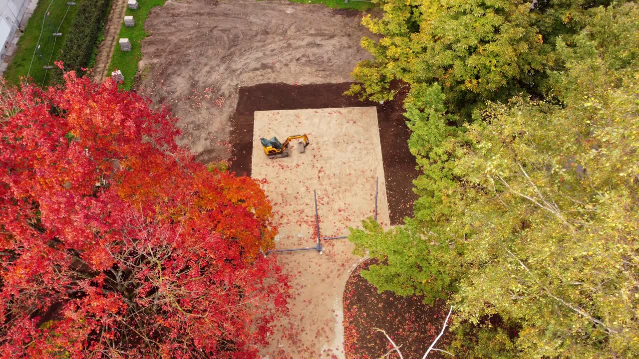 Construction site surrounded by vibrant autumn trees in a park, aerial view