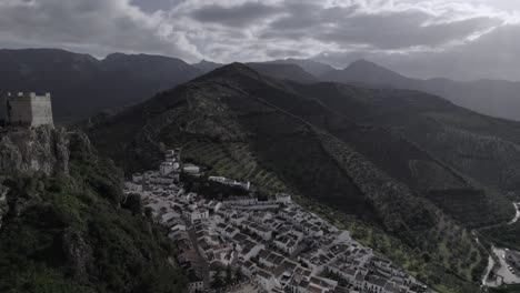 4k bird’s-eye drone shot of zahara de la sierra, spain, filmed with a dji at 30fps. a cinematic backward flight revealing the stunning medieval castle atop the mountain.
