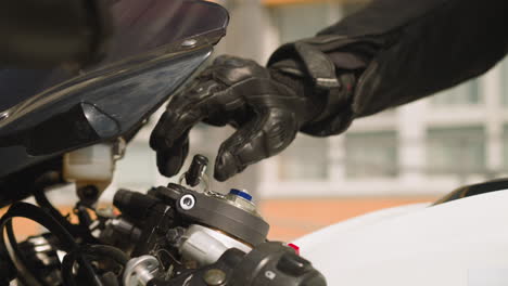 Biker-puts-key-to-ignite-motorcycle-on-parking-lot-closeup