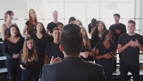 male and female students singing in choir with teacher at performing arts school