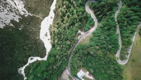 Drohnenaufnahme-Aus-Der-Vogelperspektive,-Kranabwärtsbewegung,-Bewegung-Einer-Kurvenreichen-Straße-In-Einem-Wald-Und-Vorbeifahrende-Autos