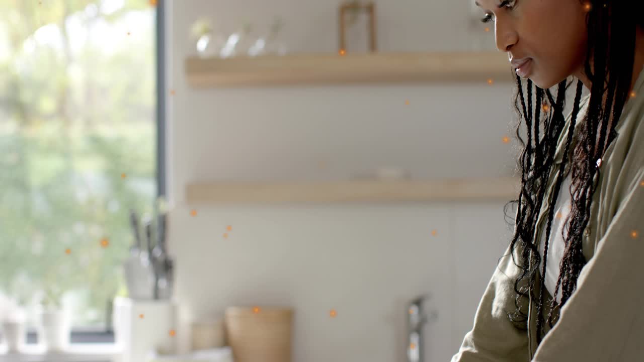 Woman typing on laptop in kitchen, orange flecks appearing and highlighting screen for remote work