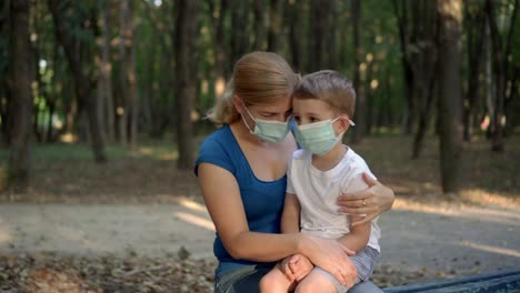 madre abraza a su hijo con máscaras médicas mientras está sentada en un parque 02