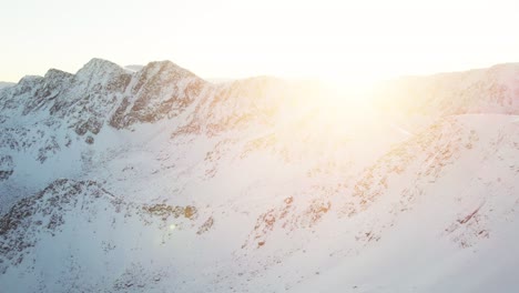 slow drone flight over snowy mountain peak at sunrise in andorra, with golden light and alpine scenery.