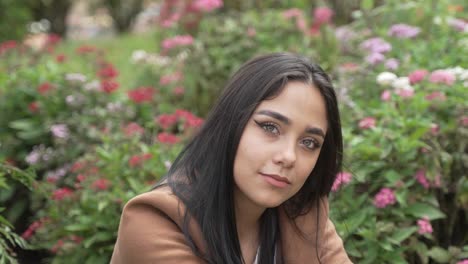 Beautiful-Green-Eyed-Latina-Woman-Sitting-infront-of-Bush-with-Roses-in-Park
