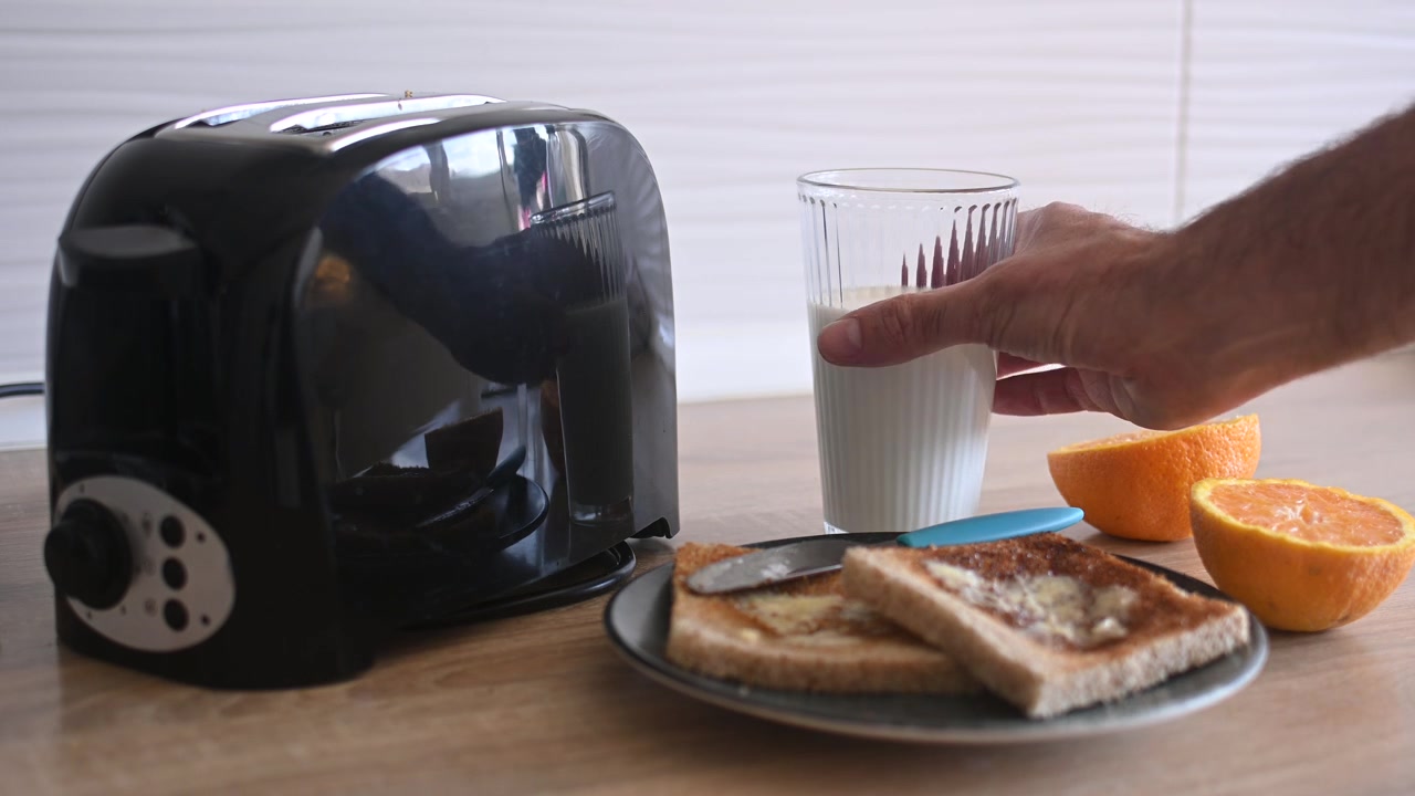 Hand picking up a glass of milk from a breakfast table
