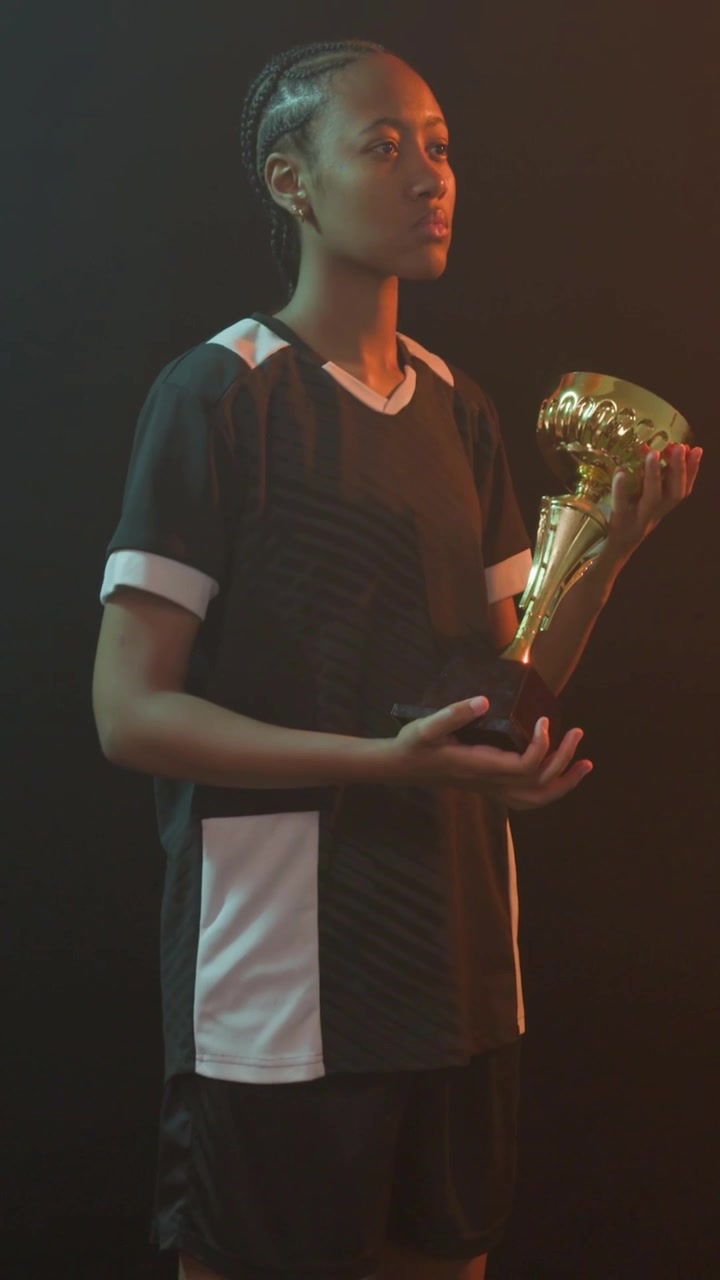 Video verticale: Atleta donna che tiene un trofeo d'oro mentre la telecamera si allontana, con luci di contorno che evidenziano la vittoria.